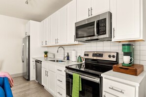A modern kitchen with white cabinets, stainless steel appliances, a coffee maker, and a dish rack. - Summer Downtown Escape, Walk to Riverwalk and Pearl, enjoy Pool + Free Parking (San Antonio)