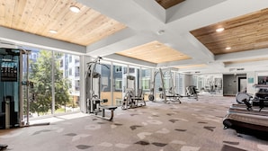 Une salle de sport spacieuse, dotée de grandes fenêtres, de divers appareils d’exercice et d’un tapis à motifs.