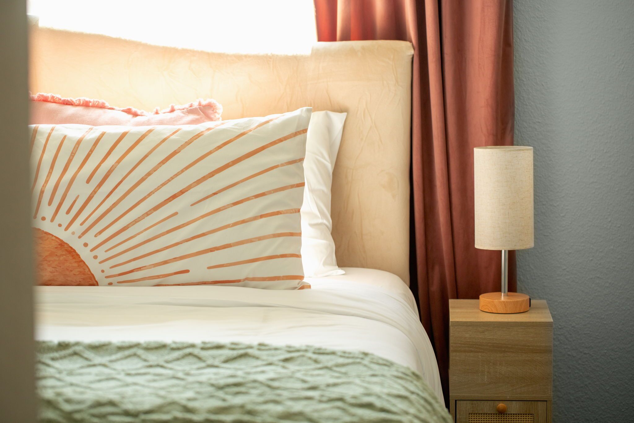 A neatly made bed with striped pillows, a bedside lamp, and a wooden nightstand.