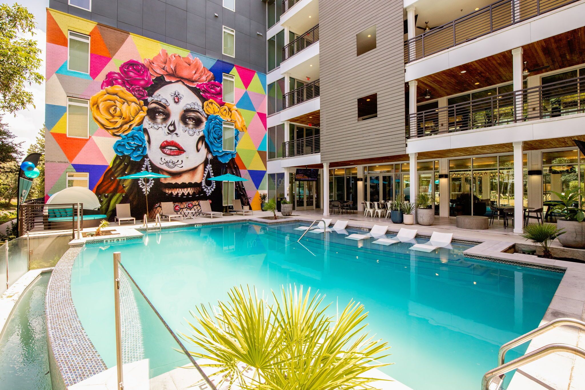 A pool area with a mural of colorful flowers and a modern building with balconies and outdoor seating.