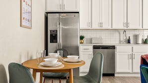 Une cuisine moderne avec des meubles blancs, des appareils en acier inoxydable et un coin repas comprenant une table et des chaises en bois.