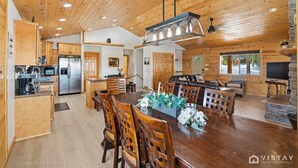 A spacious kitchen with wooden cabinets, a central island, and a dining area with a large wooden table and chairs. - Willis Woods Cabin w/ Arcades and Fire Pit (Duck Creek Village)