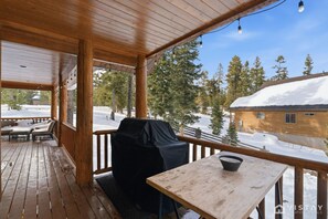 Une terrasse en bois avec un barbecue et une table, offrant une vue sur un paysage enneigé et un chalet.