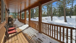 A wooden cabin with a covered porch, a fireplace, and a view of a snowy forest. - Willis Woods Cabin w/ Arcades and Fire Pit (Duck Creek Village)