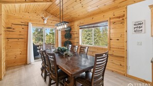A wooden cabin interior with a dining table, chairs, a chandelier, and a deer head mounted on the wall. - Willis Woods Cabin w/ Arcades and Fire Pit (Duck Creek Village)