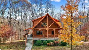 Eine Holzhütte mit Veranda, umgeben von Bäumen im Herbstlaub.