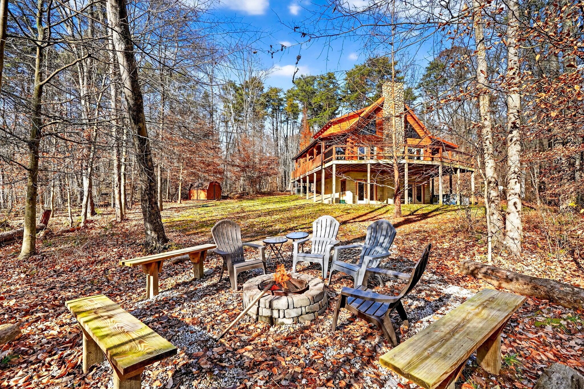 A cabin with a stone fire pit, wooden benches, and outdoor seating.