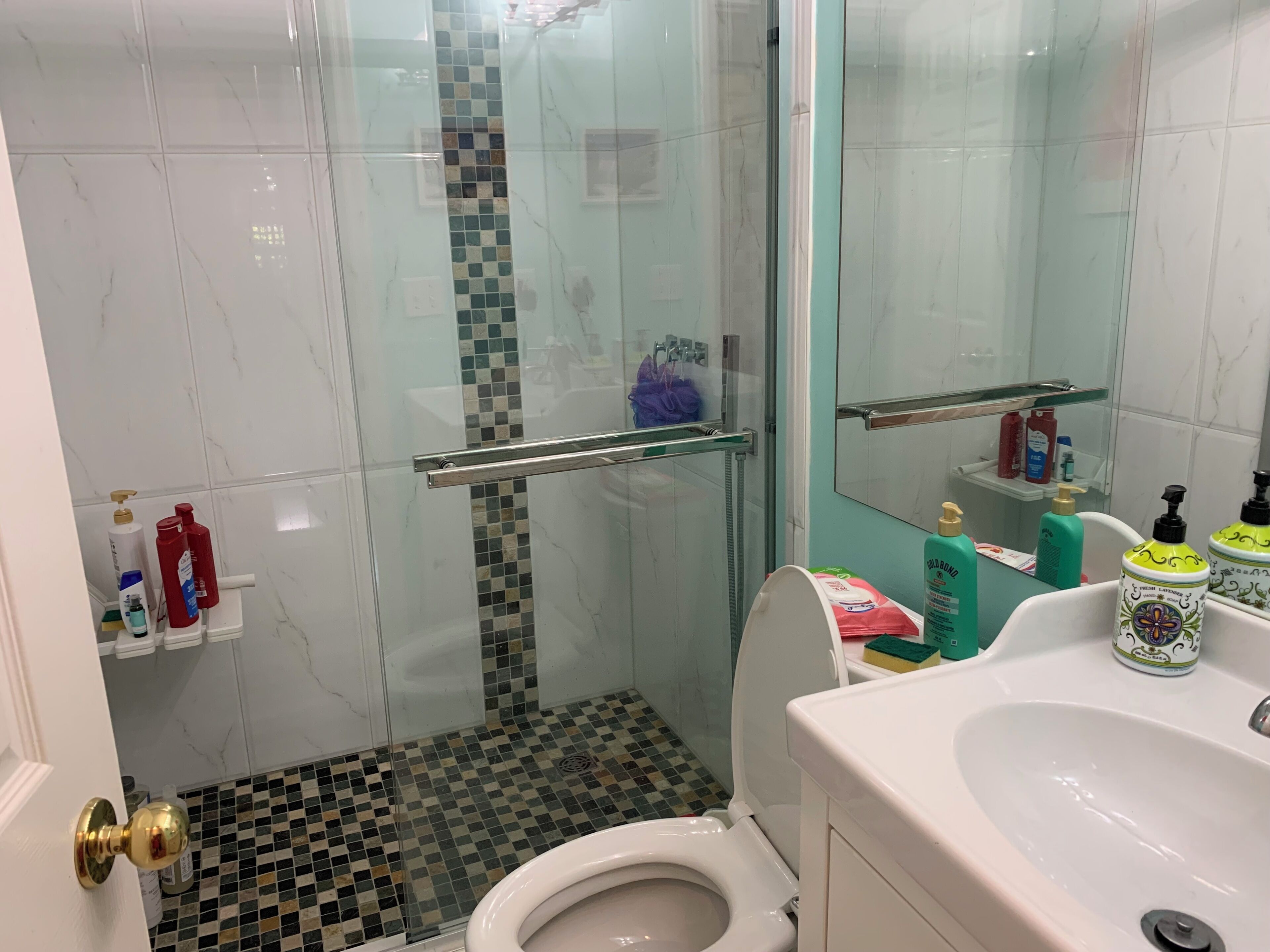 A bathroom with a glass shower enclosure, a toilet, a sink with toiletries, and a tiled floor.
