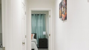 A hallway with a bed, a nightstand, and a painting on the wall.
