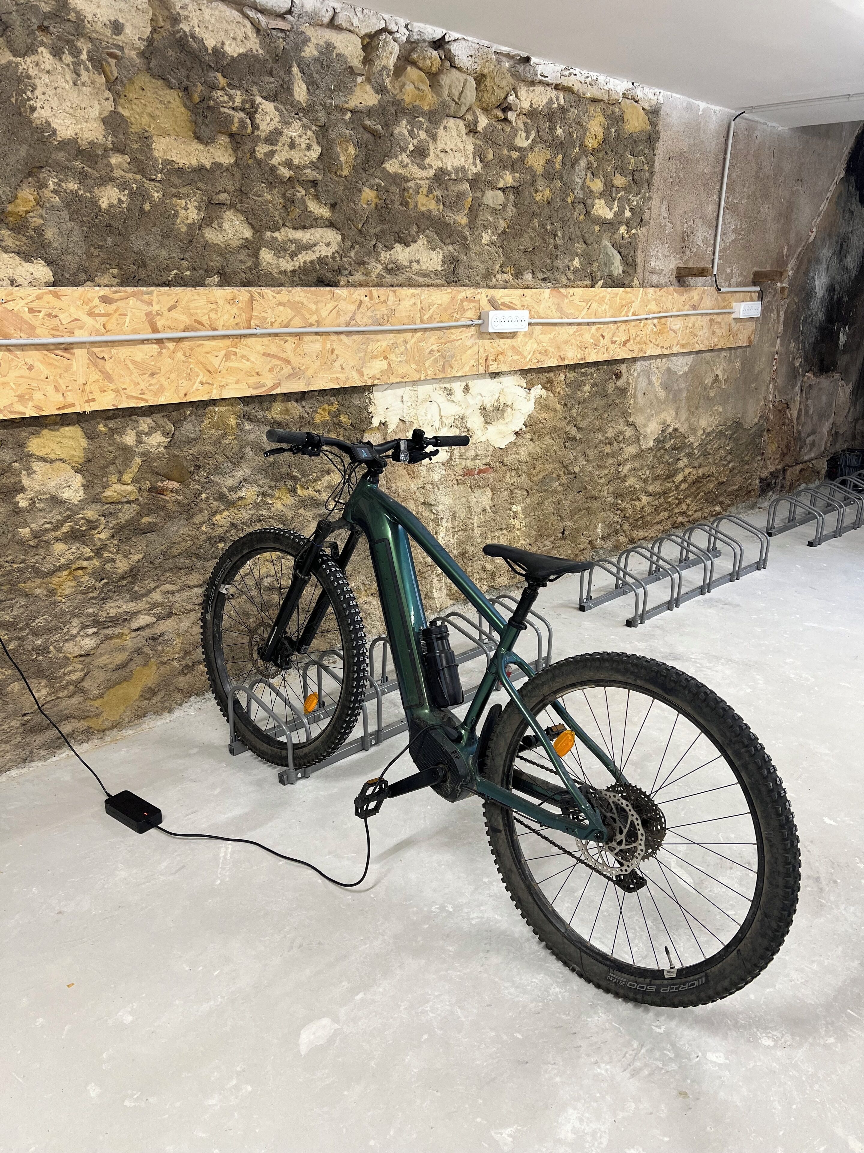 Una bicicleta estacionada junto a una pared con un estante de madera encima.