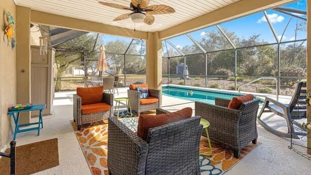 A covered outdoor area with wicker furniture, a pool, and a ceiling fan.