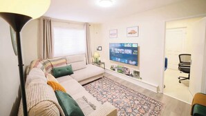 Een woonkamer met een bank, een flatscreen televisie, een kamerkleed en een lamp.