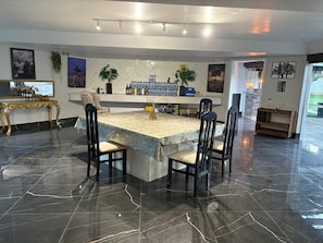 A modern kitchen with a marble countertop, four black chairs, and a bar area with bottles and glasses.