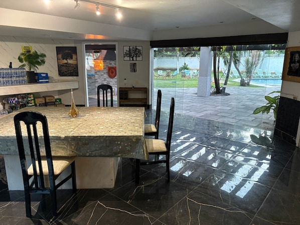 A modern dining area with a marble table and chairs, a bar area with bottles, and a view of the outdoor patio.