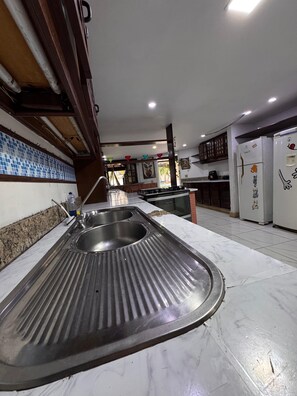 A kitchen with a stainless steel sink, a stove, cabinets, and a refrigerator.