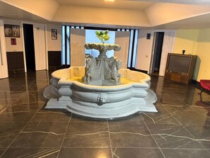 A marble-floored lobby with a central fountain featuring a horse sculpture.