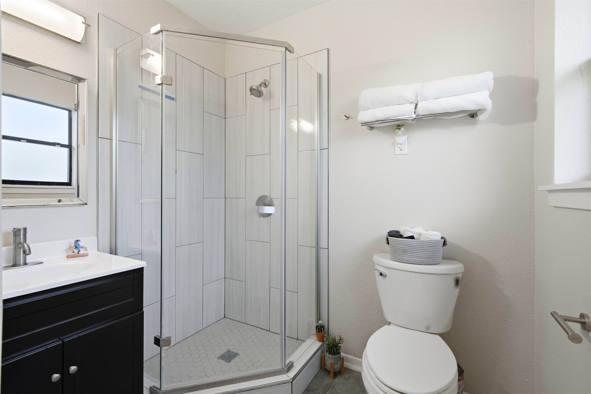 Une salle de bain moderne avec une douche à parois de verre, des toilettes blanches et un meuble-lavabo noir avec un miroir.