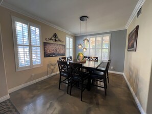 A dining area with a table and chairs, large windows with blinds, a ceiling light fixture, and a wall-mounted picture. - Dream rental home (North Las Vegas)