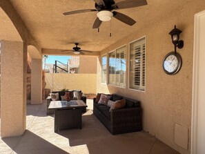 A covered patio area with a ceiling fan, a clock, and a wicker sofa. - Dream rental home (North Las Vegas)
