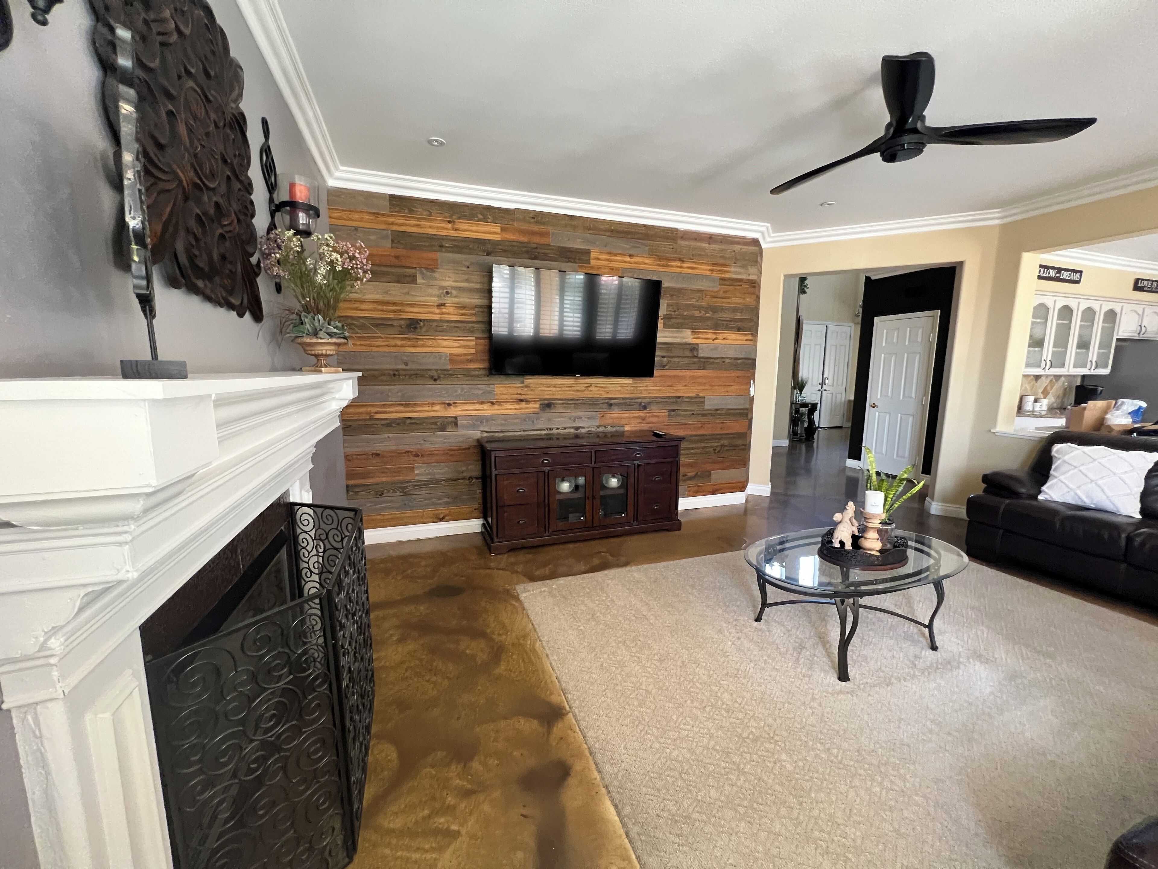 Un salon avec une cheminée, un téléviseur fixé à un mur en bois, un ventilateur de plafond et un canapé en cuir noir.