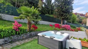 A hot tub in a garden with a stone wall, various plants, and a wooden deck. - Small Villa "The Palm" (Colazza)