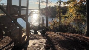 A wooden cabin with a deck overlooking a lake, surrounded by trees with autumn foliage. - Deep water, private dock, beautiful sunsets, fishing, kayaking or boating. (Gainesville)