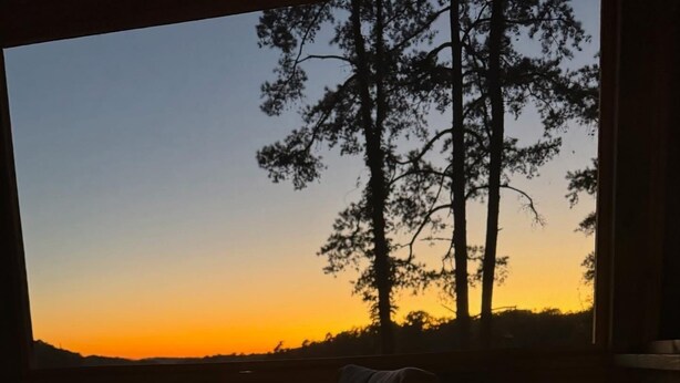 A fire pit with flames, a chair, and a view of a lake and trees at sunset. - Deep water, private dock, beautiful sunsets, fishing, kayaking or boating. (Gainesville)