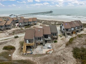 Une propriété de vacances située sur la côte, comprenant plusieurs maisons en bois, une jetée s’avançant dans l’océan et une plage de sable.