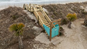 Eine Holztreppe führt zu einem Strandabschnitt mit einem Holzzaun und einer kleinen blauen Struktur.