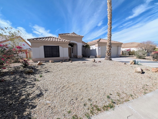 A residential property with a gravel driveway, a palm tree, and a house with a tiled roof.