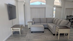 Ein geräumiges Wohnzimmer mit einem Ecksofa, einem kleinen Tisch und einem an der Wand befestigten Fernseher.