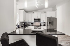 A modern kitchen with white cabinets, stainless steel appliances, and a black countertop island. - NEW LISTING Amazing Location! 4BR, Pool, Mid-Term Stays! Close to Disney! (Davenport)