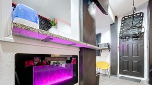 Un ambiente compatto con angolo salotto integrato, un piccolo tavolo da pranzo e una porta con cancello in metallo.
