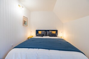 Un dormitorio con cama, dos lámparas de noche, un cuadro enmarcado en la pared y techo inclinado.
