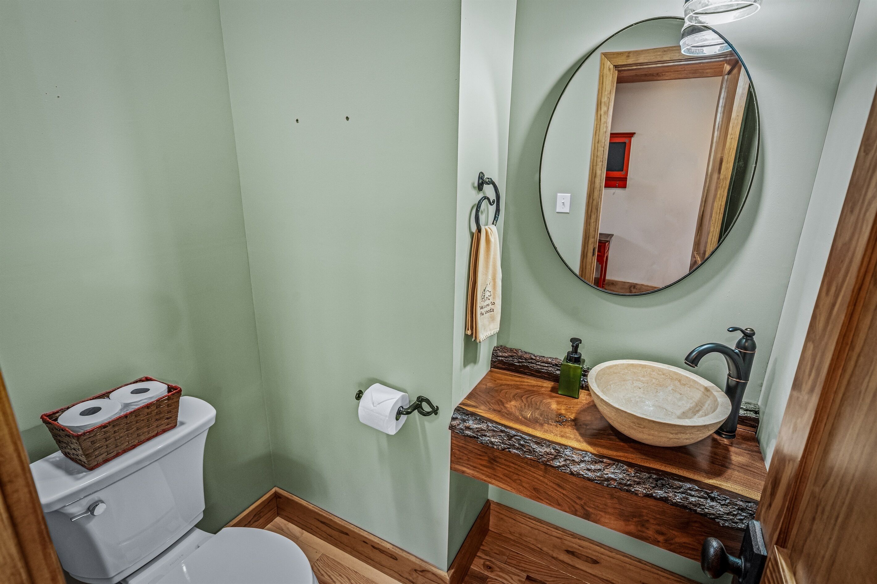 A bathroom with a toilet, a wooden vanity with a sink, a mirror, and a towel rack.