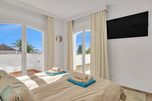 A hotel room with a bed, a TV mounted on the wall, and a view of the outside. - Villa Molly - Elegant Beachside Home (Marbella)