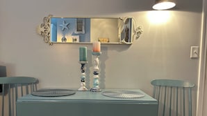 Une table à manger de couleur turquoise, accompagnée de deux chaises, un miroir doté d’un cadre orné et deux chandeliers avec des bougies turquoise.