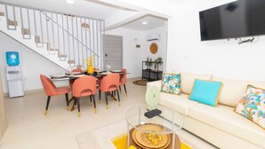 Una sala de estar moderna con un sofá, un comedor con sillas, una escalera y un televisor de pantalla plana montado en la pared.