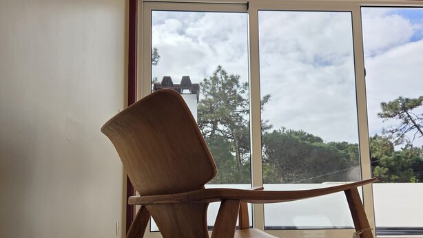 A wooden chair in a room with large windows, wooden flooring, and a light fixture on the wall. - Villa do Canal (Apúlia)