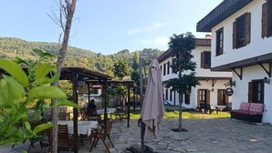 An outdoor patio with stone flooring, wooden tables and chairs, and a covered seating area. - İkiz Konaklar (Şirince)