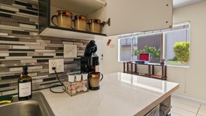 Een moderne keuken met een aanrecht, een koffiezetapparaat, een fles afwasmiddel en een raam met uitzicht op een rode stoel en groen buiten.