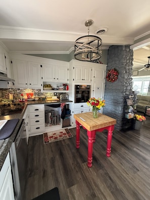 A modern kitchen with white cabinets, a stone accent wall, a wooden table with a vase of flowers, and a red chair.