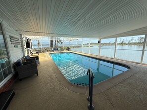 An indoor swimming pool with a view of a lake, surrounded by seating and a covered area.