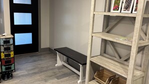 A room with a wooden bench, a white shelving unit with picture frames, and a door with frosted glass panels.