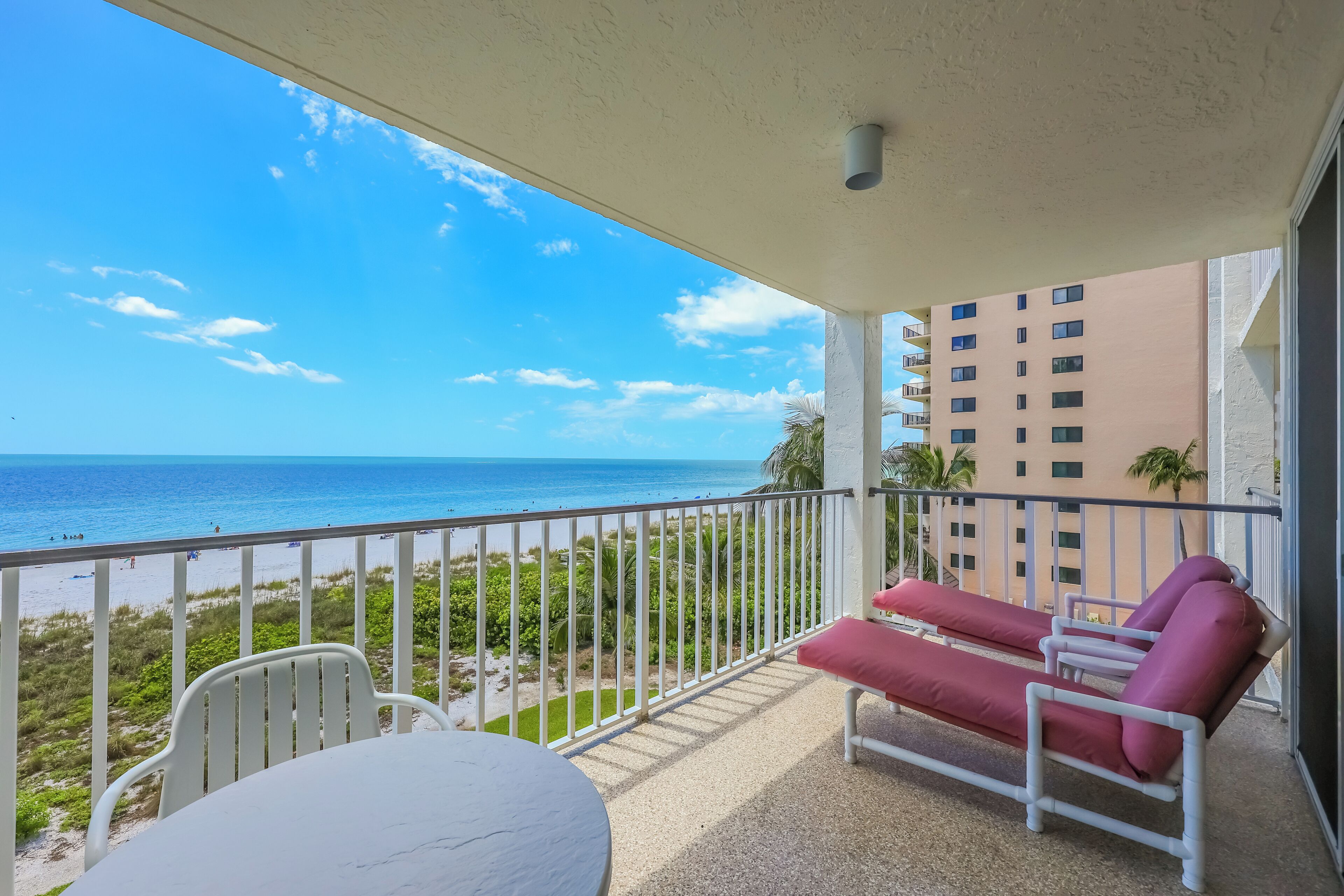 Un balcone con tavolo e sedie, una poltrona reclinabile rossa e vista sulla spiaggia e l'oceano.