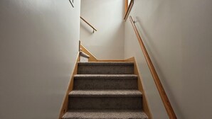 Un escalier recouvert de moquette, doté de rampes en bois, menant à un palier éclairé par un luminaire.