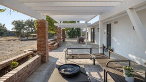 Eine überdachte Terrasse im Freien mit Feuerstelle, Sitzgelegenheiten und Blick auf die umliegende Landschaft.