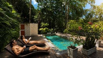 A poolside area with two lounge chairs, a stone wall, and lush greenery.