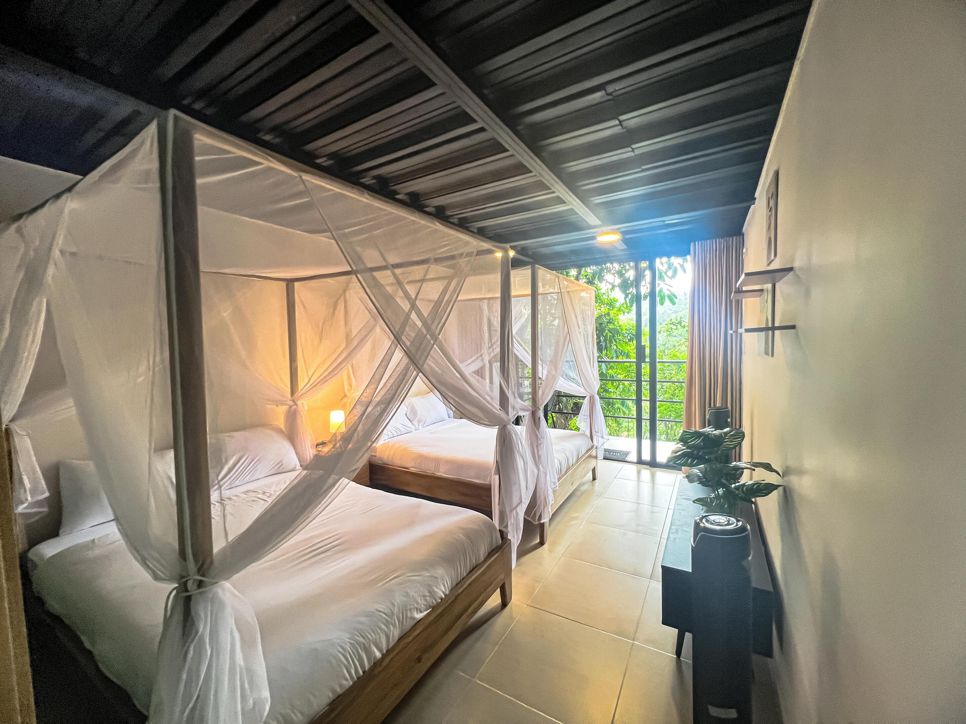 Ein Zimmer mit zwei Betten, jeweils mit Baldachin, einem kleinen Tisch und Blick auf Grünflächen.