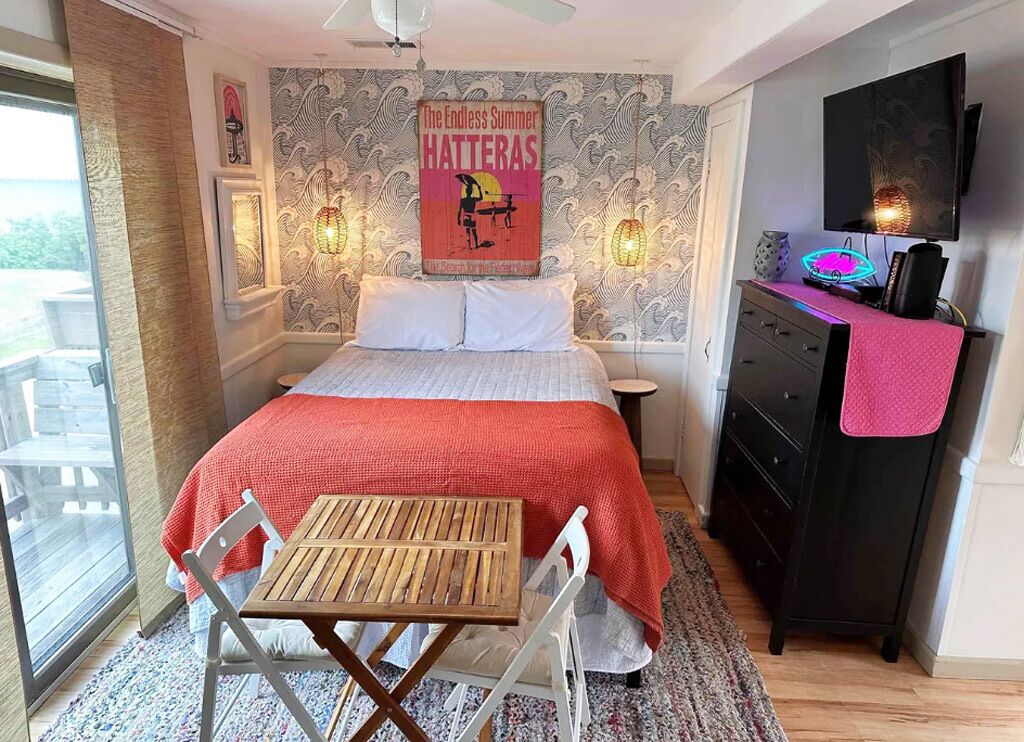 Une chambre à coucher avec un lit, un bureau et une chaise. Il y a un téléviseur accroché au mur et une fenêtre avec des rideaux.